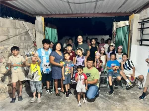 Group of adults and children posing in an open garage with concrete floor and walls