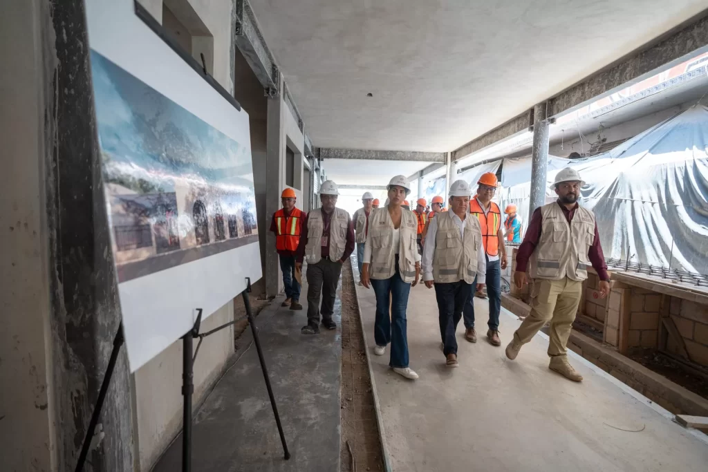 Grupo de personas con chalecos y cascos revisando obra en construcción con planos visibles