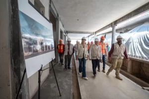 Grupo de personas con chalecos y cascos revisando obra en construcción con planos visibles