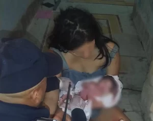 Mujer con un recién nacido y un hombre que parece ayudar en un parto en un lugar cerrado