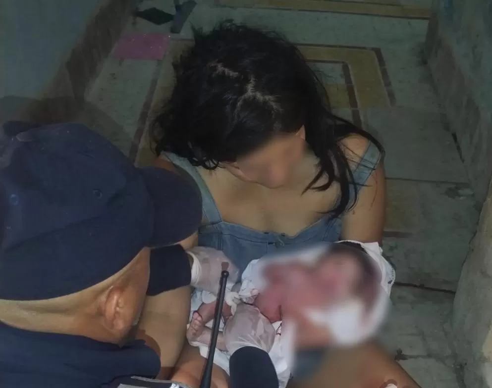 Mujer con un recién nacido y un hombre que parece ayudar en un parto en un lugar cerrado
