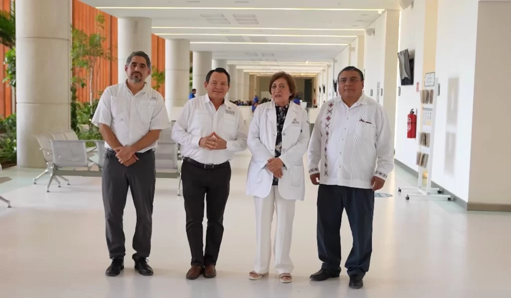 Cuatro personas de pie en pasillo amplio y luminoso de hospital o clínica