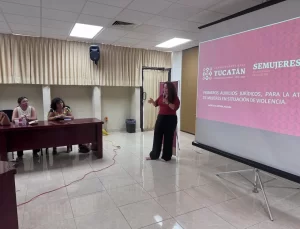 Mujer dando presentación con micrófono frente a una pantalla con texto sobre primeros auxilios jurídicos para mujeres en situ