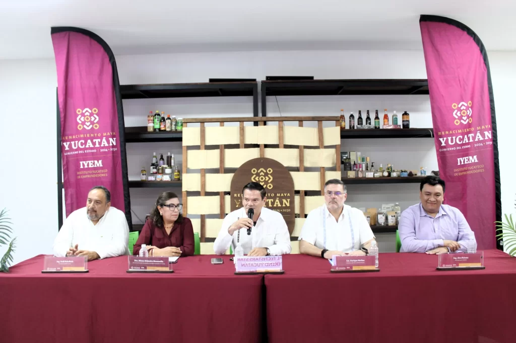 Cinco personas sentadas en mesa con manteles rojos en conferencia del Instituto Yucateco de Emprendedores