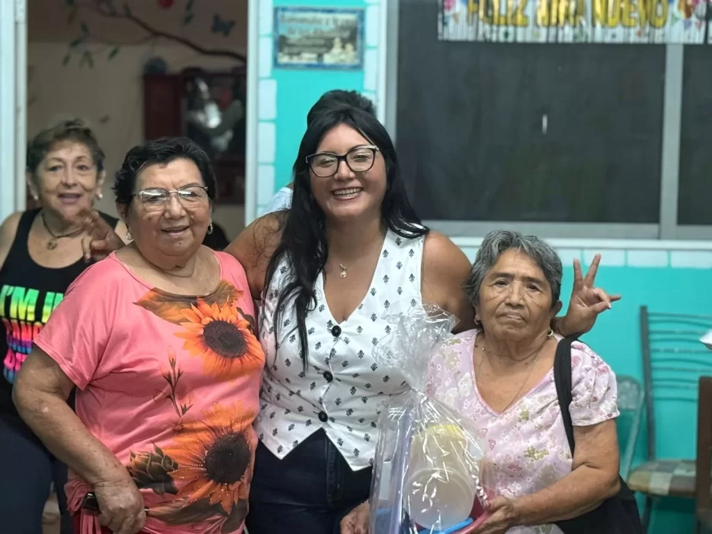 Tres mujeres sonrientes posando juntas, una sostiene un paquete envuelto en plástico