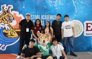 Siete jóvenes posando con la mascota de ECyTE Quintana Roo en Festival Académico en fondo azul