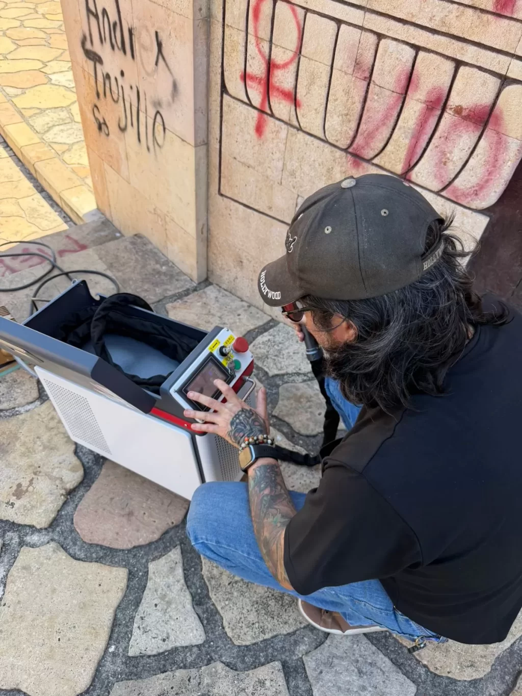 Hombre con gorra negra y tatuajes usando una máquina con pantalla táctil en un piso de piedra