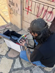 Hombre con gorra negra y tatuajes usando una máquina con pantalla táctil en un piso de piedra