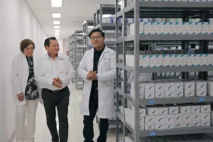 Tres personas caminando junto a estantes llenos de cajas de medicamentos en una bodega