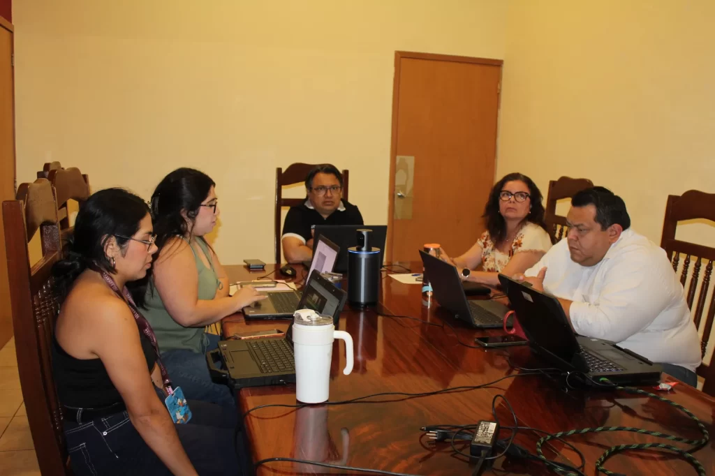 Cinco personas sentadas alrededor de una mesa de madera usando laptops