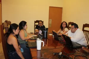 Cinco personas sentadas alrededor de una mesa de madera usando laptops