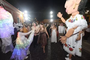 Mujeres y hombres participando en evento cultural nocturno con personajes gigantes y luces