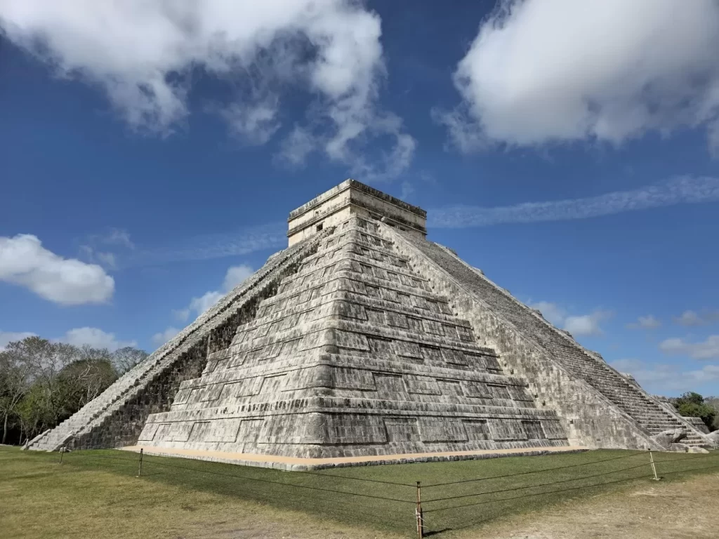 Vista lateral de la pirámide de Chichén Itzá con cielo azul y algunas nubes