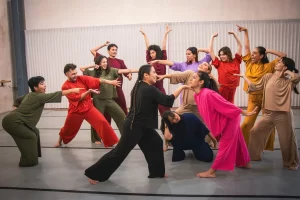 Doce bailarines en ropa cómoda de colores realizando una coreografía en estudio