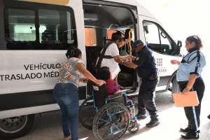 Personal de apoyo ayudando a una mujer de la tercera edad a subir a una camioneta de traslado médico mientras otra persona es