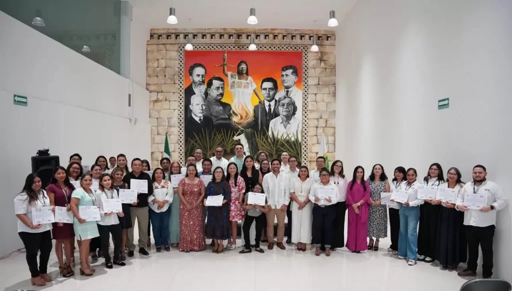 Grupo de personas posando con certificados frente a mural en salón amplio y blanco