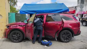 Policía municipal inspecciona una SUV roja que presenta daños en la puerta delantera y lateral