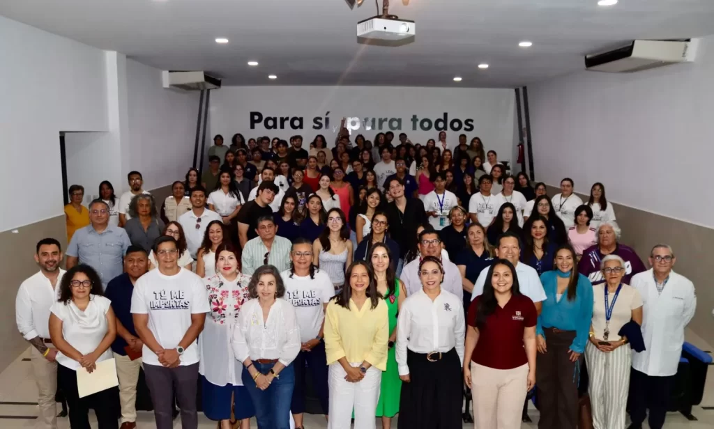 Grupo numeroso de personas en salón con letrero al fondo que dice 'Para sí y para todos'