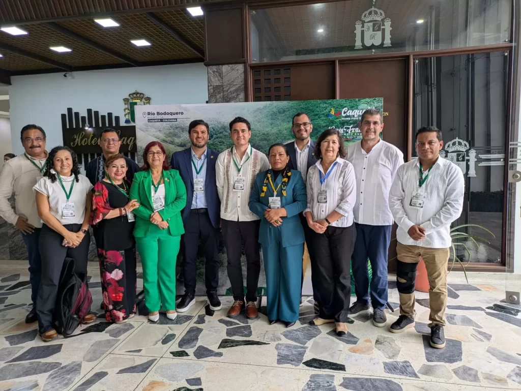 Doce personas posando en grupo dentro de un hotel, con gafetes colgados y vestimenta formal y casual