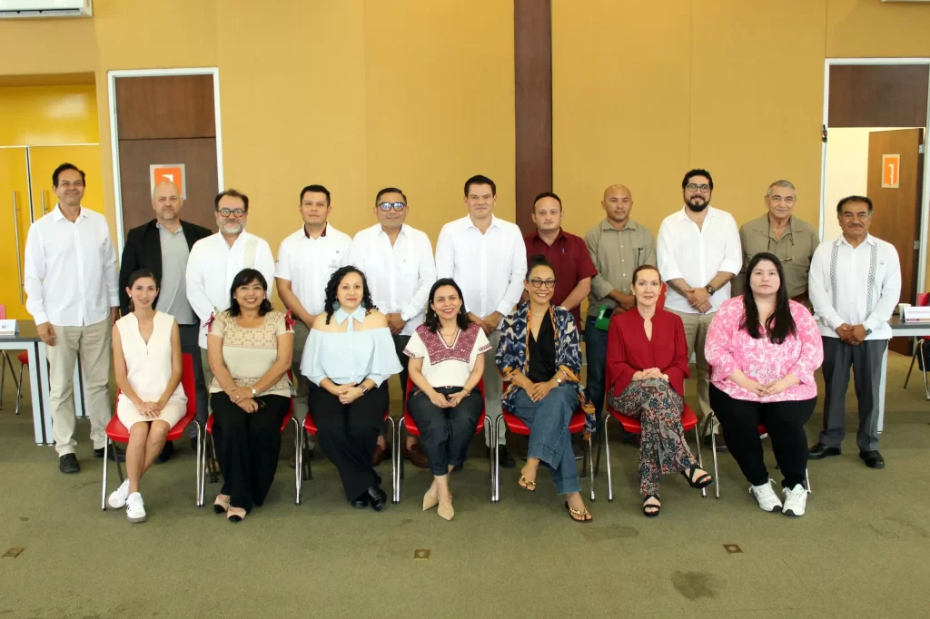 Grupo de 17 personas posando en ambiente interior con paredes amarillas
