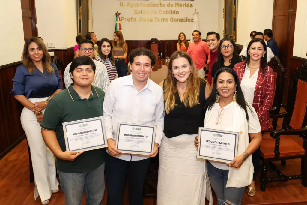 Grupo de personas en salón de cabildo del Ayuntamiento de Mérida posando con reconocimientos en mano