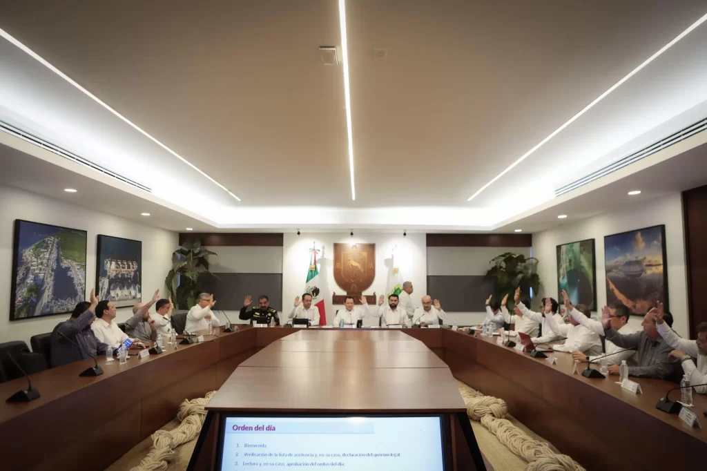 Integrantes del cabildo de Yucatán levantan la mano durante sesión en sala de juntas moderna