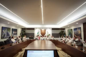 Integrantes del cabildo de Yucatán levantan la mano durante sesión en sala de juntas moderna
