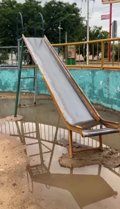 Tobogán metálico oxidado y desgastado con charcos de agua en el suelo de un parque