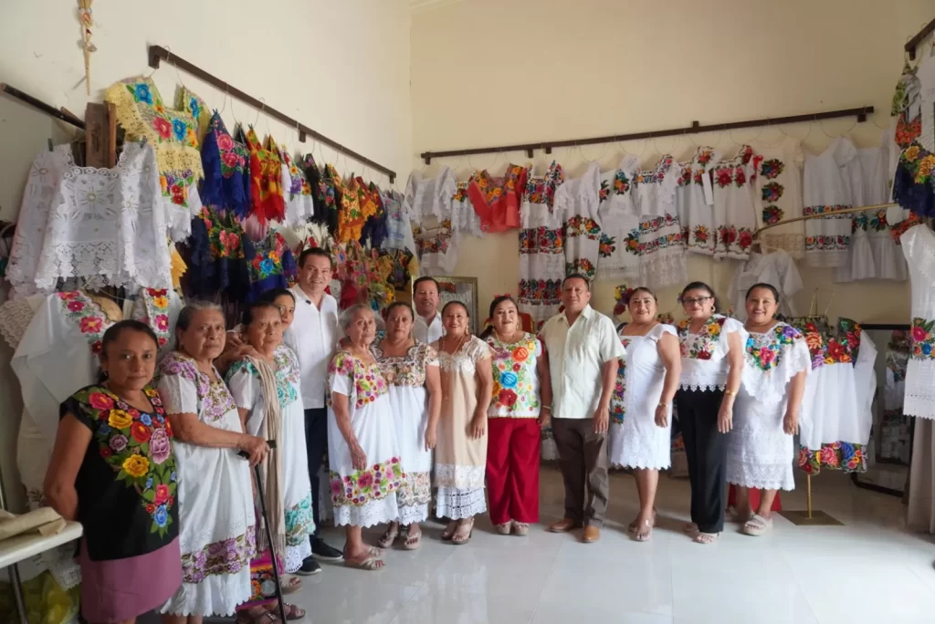 Personas posando en una habitación con vestidos tradicionales bordados colgados en la pared