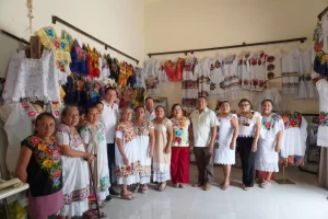 Personas posando en una habitación con vestidos tradicionales bordados colgados en la pared