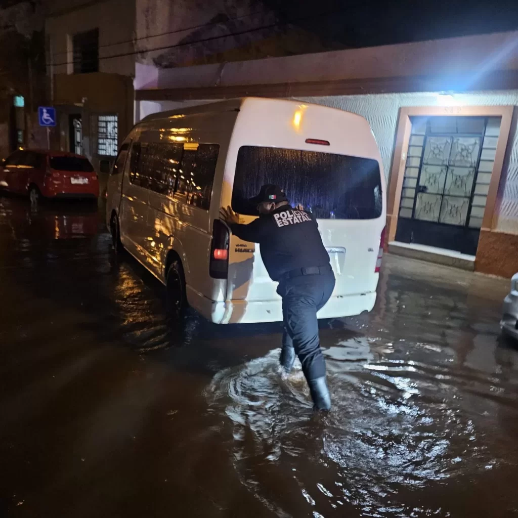 Policía estatal con botas empujar una camioneta blanca en calle inundada por lluvia en la noche