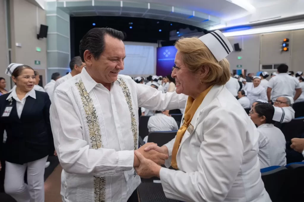 Hombre con camisa típica saludando alegremente a enfermera con uniforme blanco en auditorio