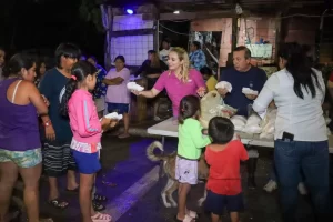 Personas entregando alimentos a niños y adultos en espacio abierto por la noche
