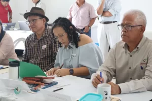 Cuatro personas en una reunión tomando notas y con laptop en mesa blanca