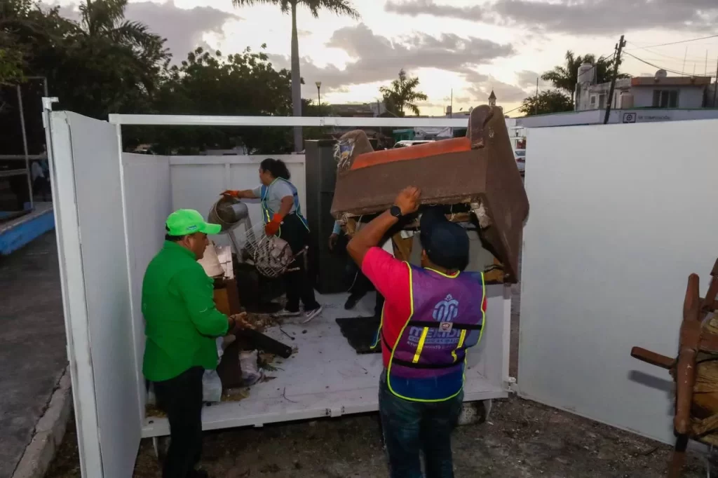 Personas recogiendo muebles y objetos en un contenedor metálico blanco al aire libre