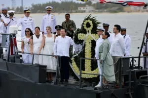 Personas en ceremonia naval sobre un bote con ofrenda floral en forma de ancla