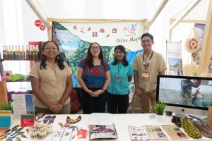 Cuatro personas sonrientes frente a un puesto con artesanías y un cartel de Co'ox Mayab