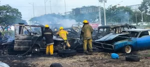 Equipo de bomberos en acción apagando el incendio de varios vehículos quemados