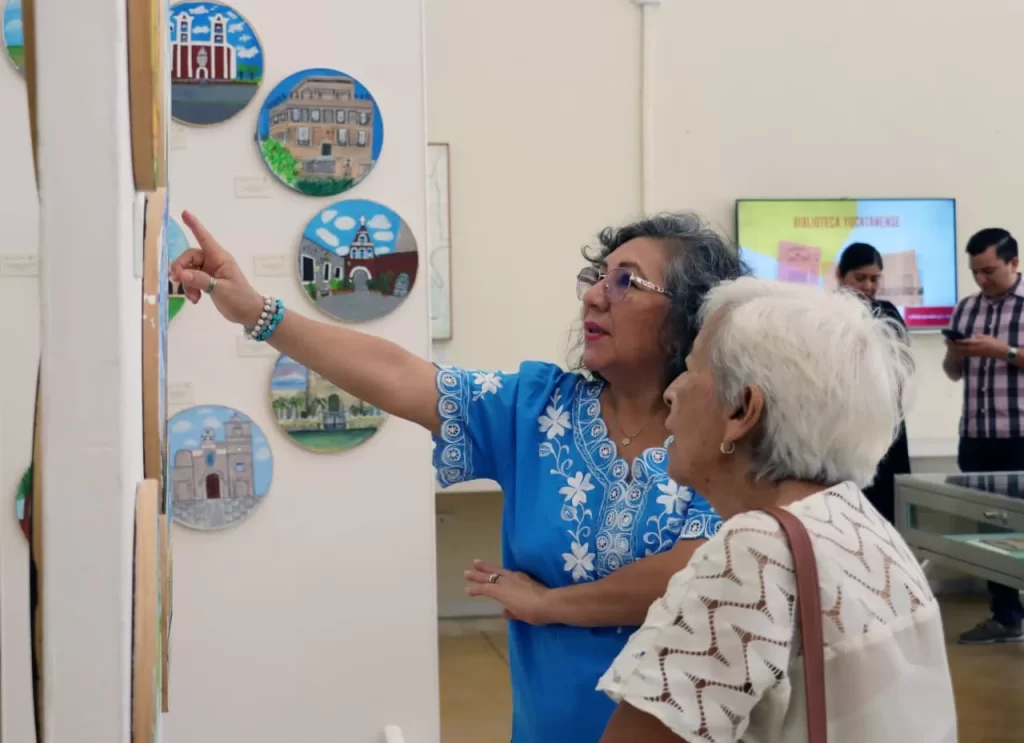 Dos mujeres observando y señalando una pintura en una galería con cuadros redondos en la pared