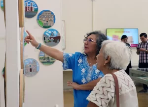 Dos mujeres observando y señalando una pintura en una galería con cuadros redondos en la pared