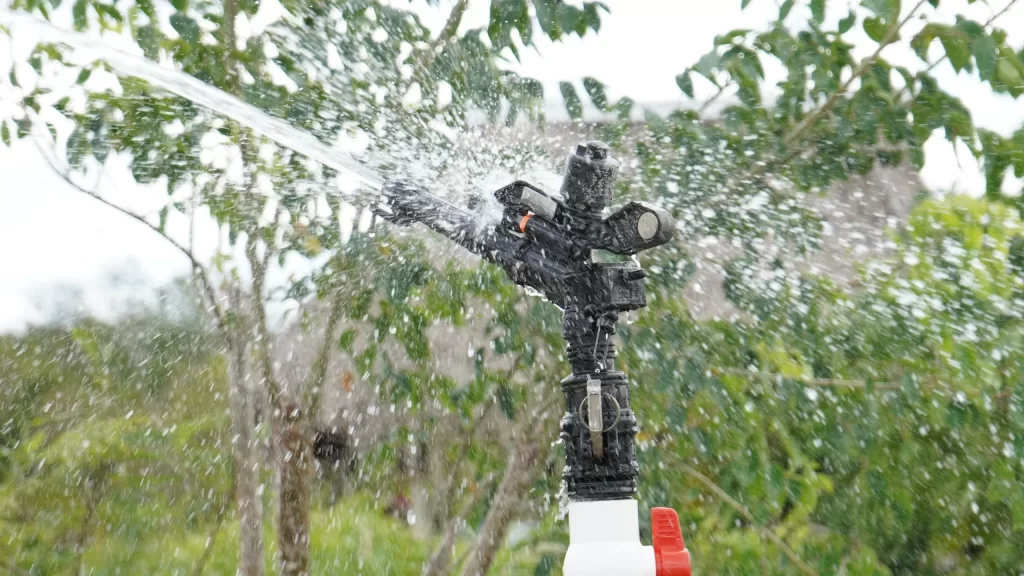 Aspersor negro rociando agua con árboles verdes al fondo