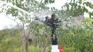 Aspersor negro rociando agua con árboles verdes al fondo