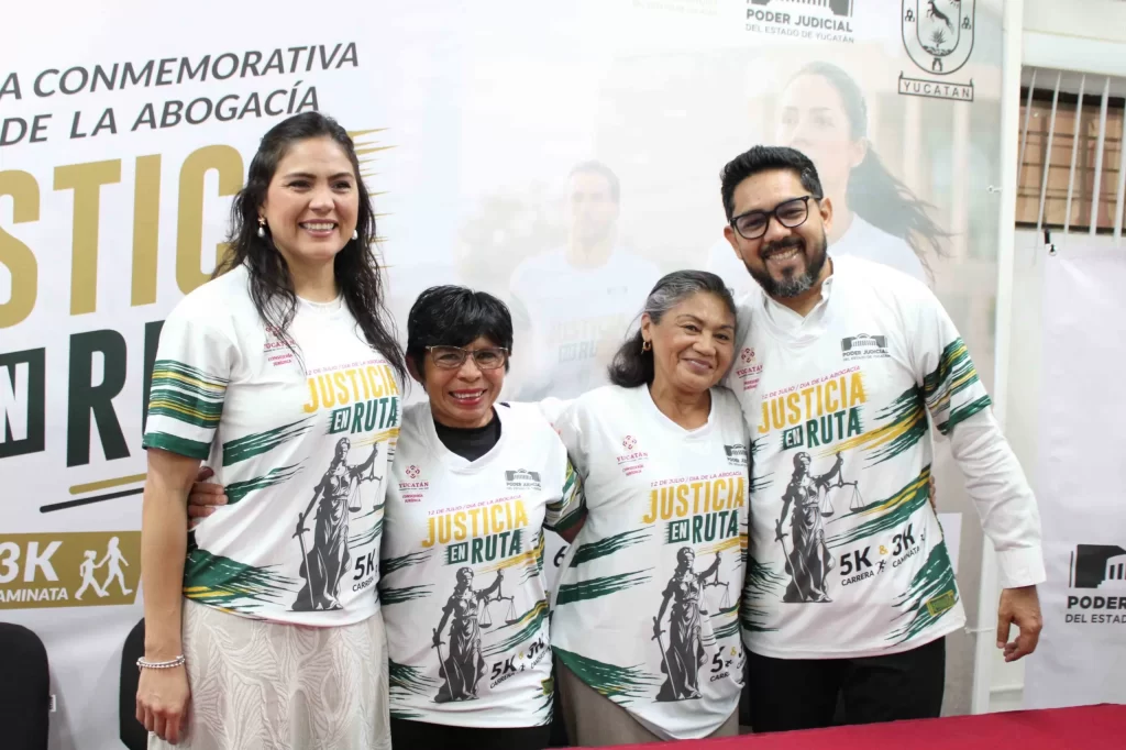 Cuatro personas sonrientes usando camisetas con el texto Justicia en Ruta, posando frente a un cartel del Poder Judicial de Y