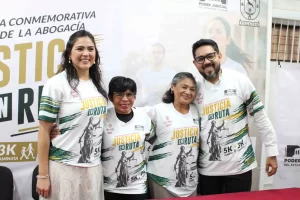 Cuatro personas sonrientes usando camisetas con el texto Justicia en Ruta, posando frente a un cartel del Poder Judicial de Y