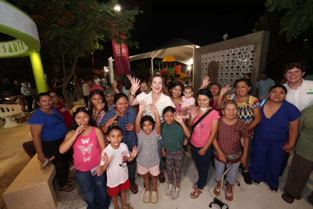 Grupo de personas de varias edades sonriendo y saludando en un parque iluminado por la noche