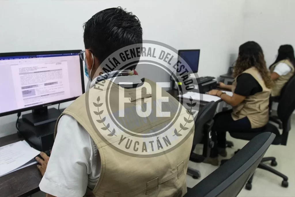 Tres personas con chalecos beige trabajando en computadoras en oficina