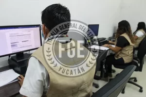 Tres personas con chalecos beige trabajando en computadoras en oficina