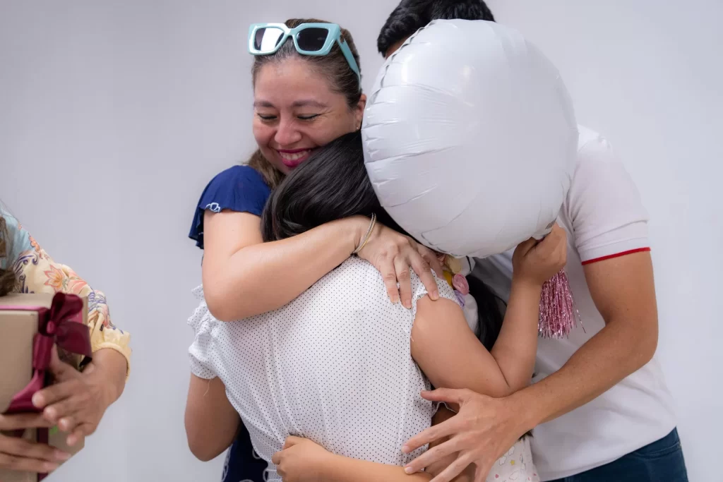 Personas abrazándose en celebración, una con gafas azules y globo blanco