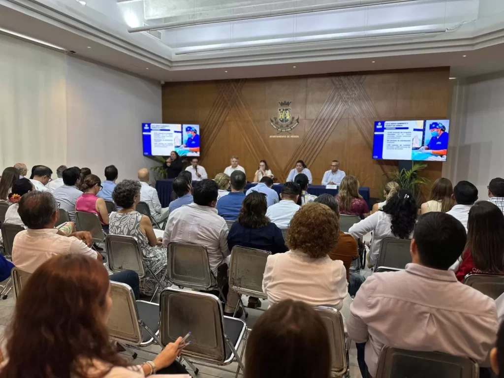 Personas sentadas en una sala viendo presentación en dos pantallas en Ayuntamiento de Mérida