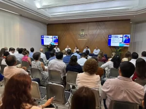 Personas sentadas en una sala viendo presentación en dos pantallas en Ayuntamiento de Mérida